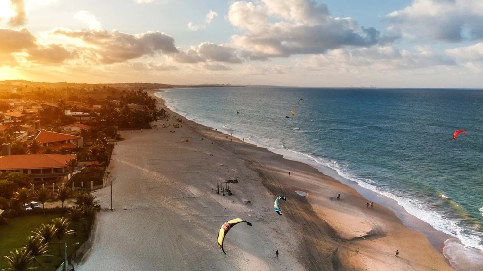 Fotografia real da orla de Cumbuco, com praia, coqueiros e mar